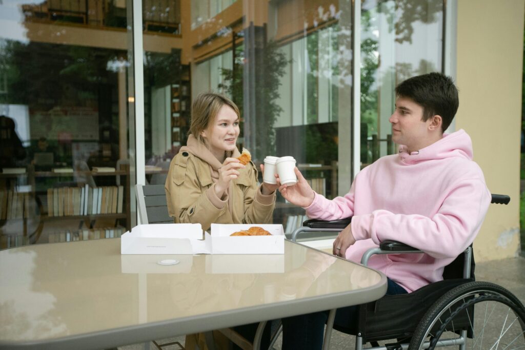 pexels photo 8416030 8416030 Two friends enjoying coffee and croissants, one in a wheelchair, outdoors.